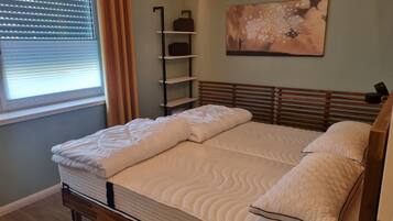 Ein ordentlich bezogenes Bett mit Holz-Kopfteil, einem an der Wand montierten Regal und einem Gemälde darüber.