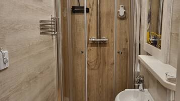 Ein modernes Badezimmer mit einer Glaskabine zur Dusche, einem weißen Waschbecken und einem Holzlagerraum.