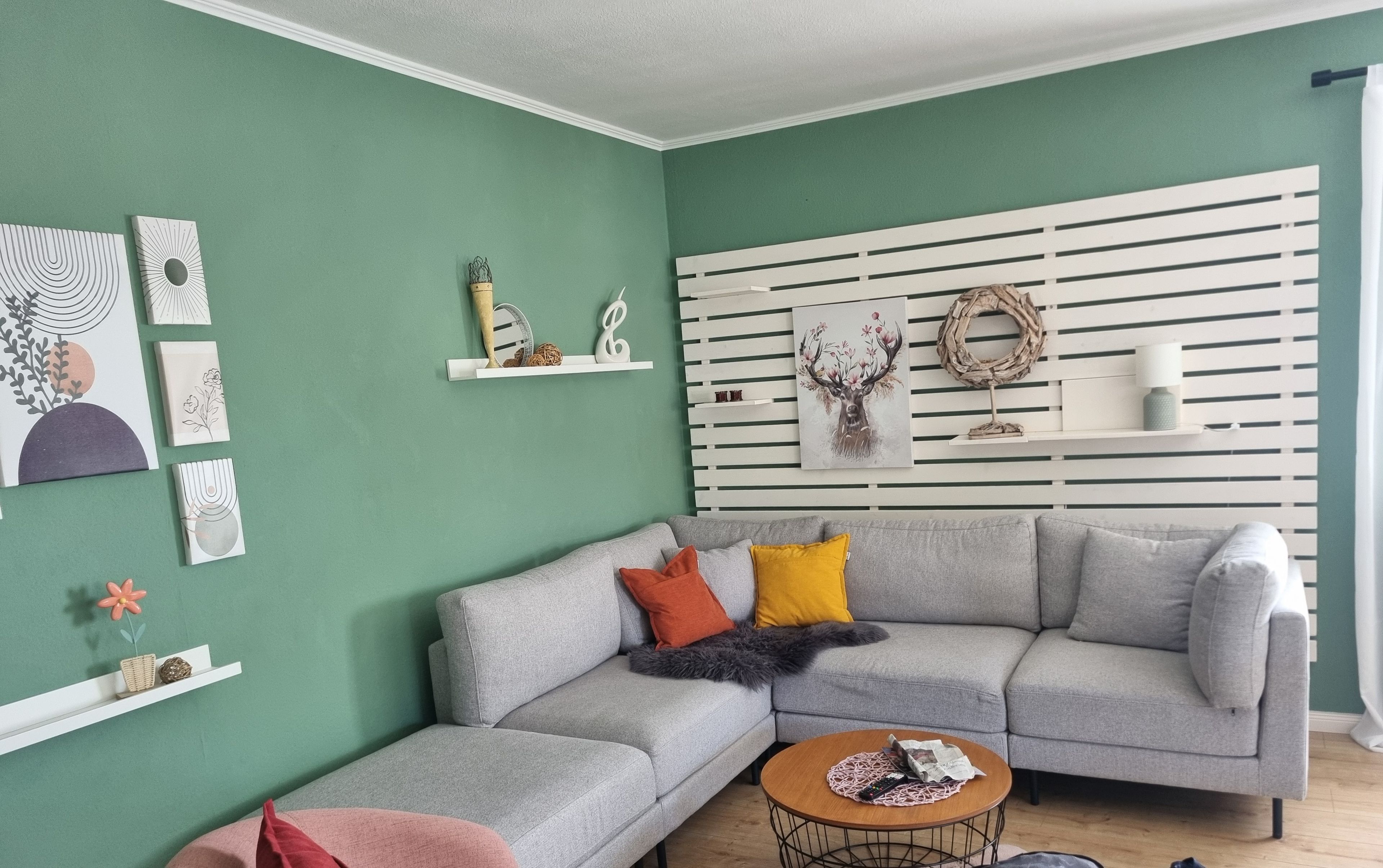 Ein modernes Wohnzimmer mit einem grauen Ecksofa, einem runden Couchtisch und einer weißen Wandschränke mit dekorativen Elementen.