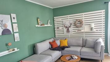 Ein modernes Wohnzimmer mit einem grauen Ecksofa, einem runden Couchtisch und einer weißen Wandschränke mit dekorativen Elementen.