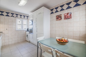 A kitchen with white cabinets, a built-in oven, a washing machine, and a dining table with chairs.