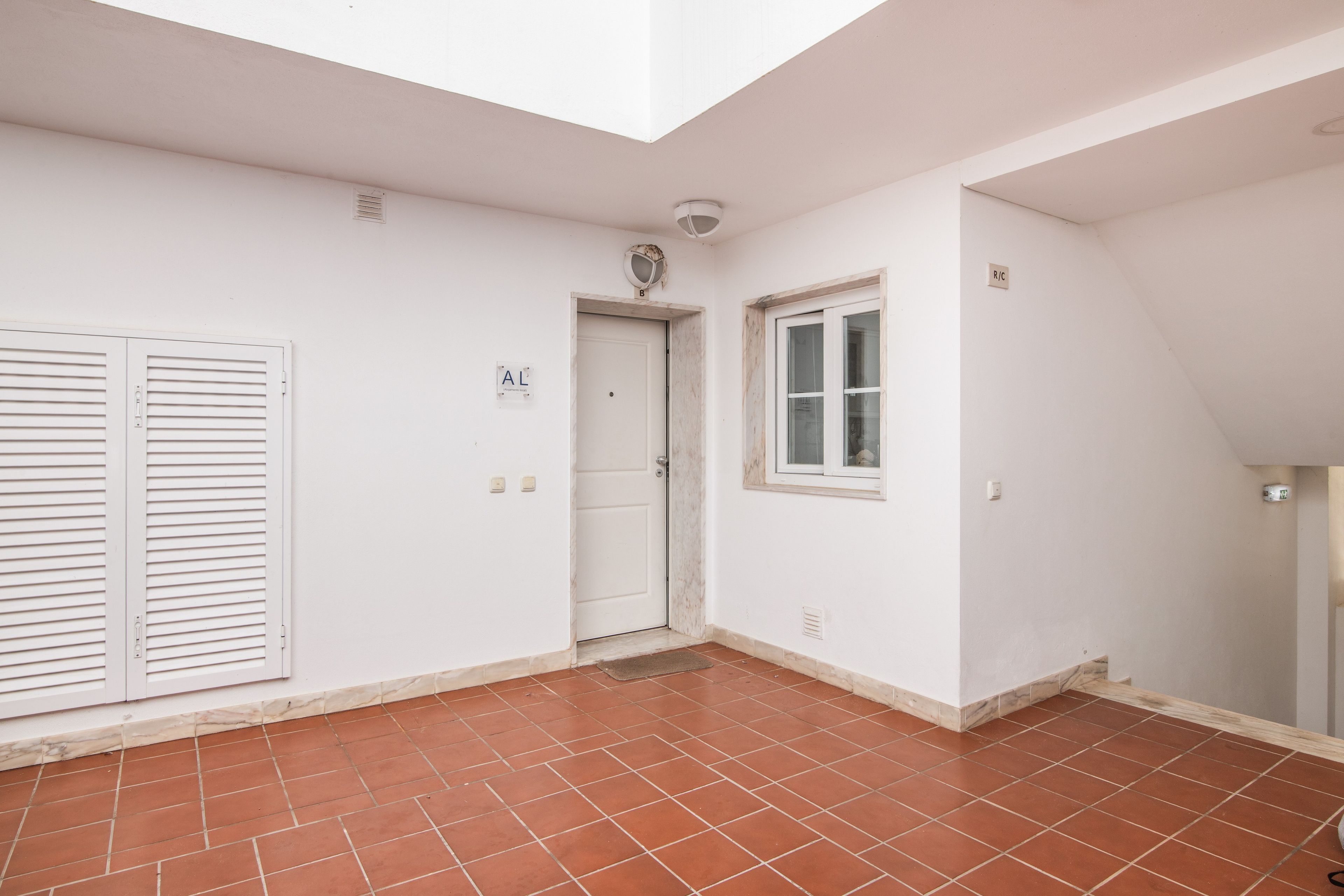 Une pièce avec un sol carrelé, une porte blanche, une fenêtre et un luminaire au plafond.