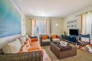 A living room with a sofa, armchairs, a coffee table, a flat-screen TV, and a wall-mounted TV.