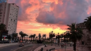 A sunset over a city street with buildings and palm trees. - Azzuro Apartment in Durr s (Durrës)