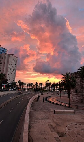 A sunset over a city street with buildings and palm trees. - Azzuro Apartment in Durr s (Durrës)