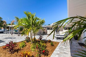 A courtyard with palm trees, a pool, and lounge chairs. - Beachside Bungalow - Unit A | 2BR, 8-Min Walk to Beach, Patio & BBQ Grills 🌴 (Cape Canaveral)