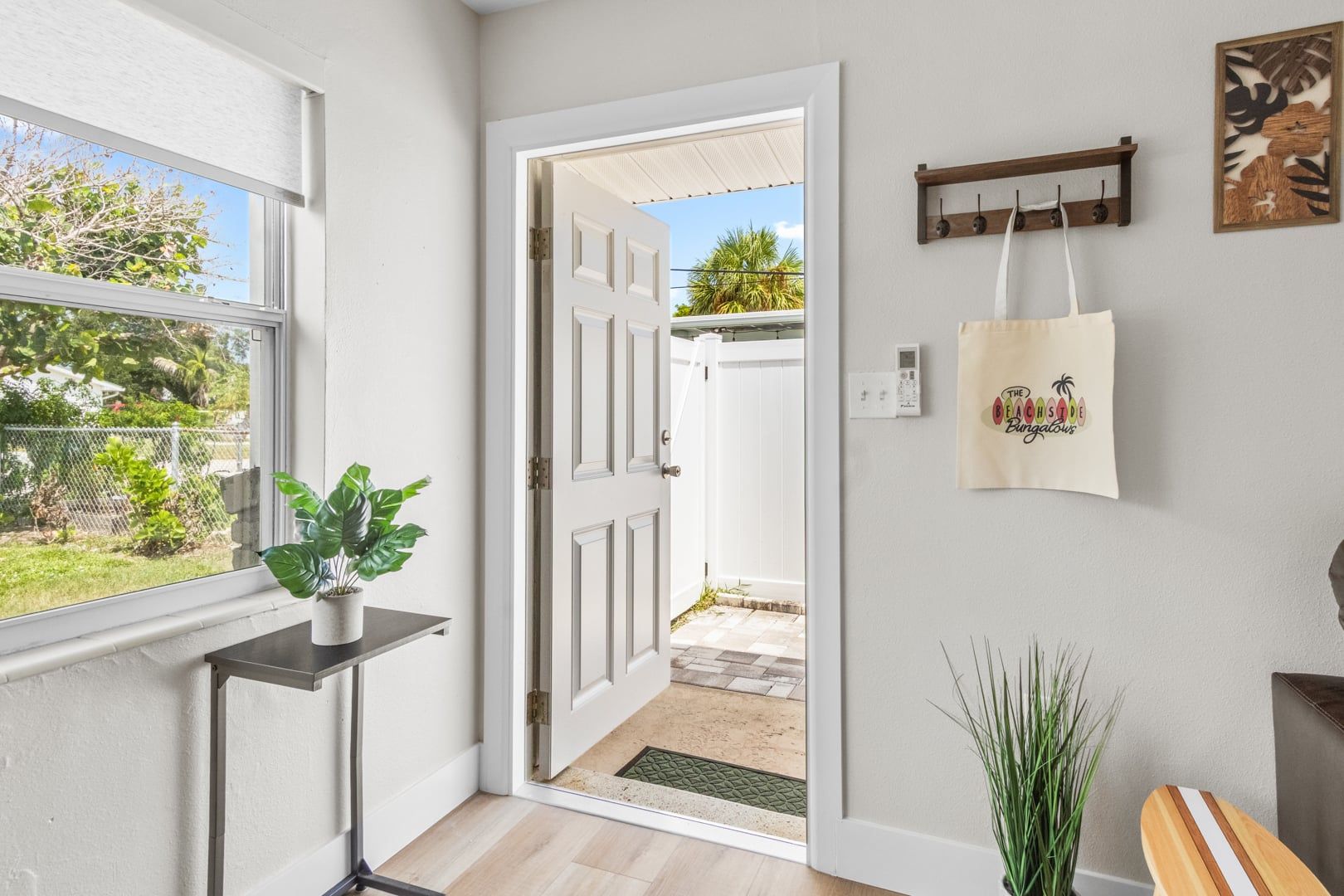 A hallway with a door leading to a backyard, a potted plant, a wall-mounted bag rack, and a small table.