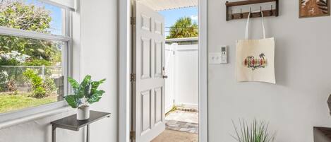 A hallway with a door leading to a backyard, a potted plant, a wall-mounted bag rack, and a small table.