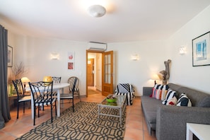 Ein Wohnzimmer mit einer Couch, Sesseln, einem Esstisch und einem gemusterten Teppich.