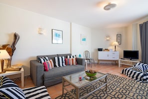 Ein modernes Wohnzimmer mit einem grauen Sofa, gestreiften Kissen, einem Glastisch, einem Fernseher und einem Schrank.