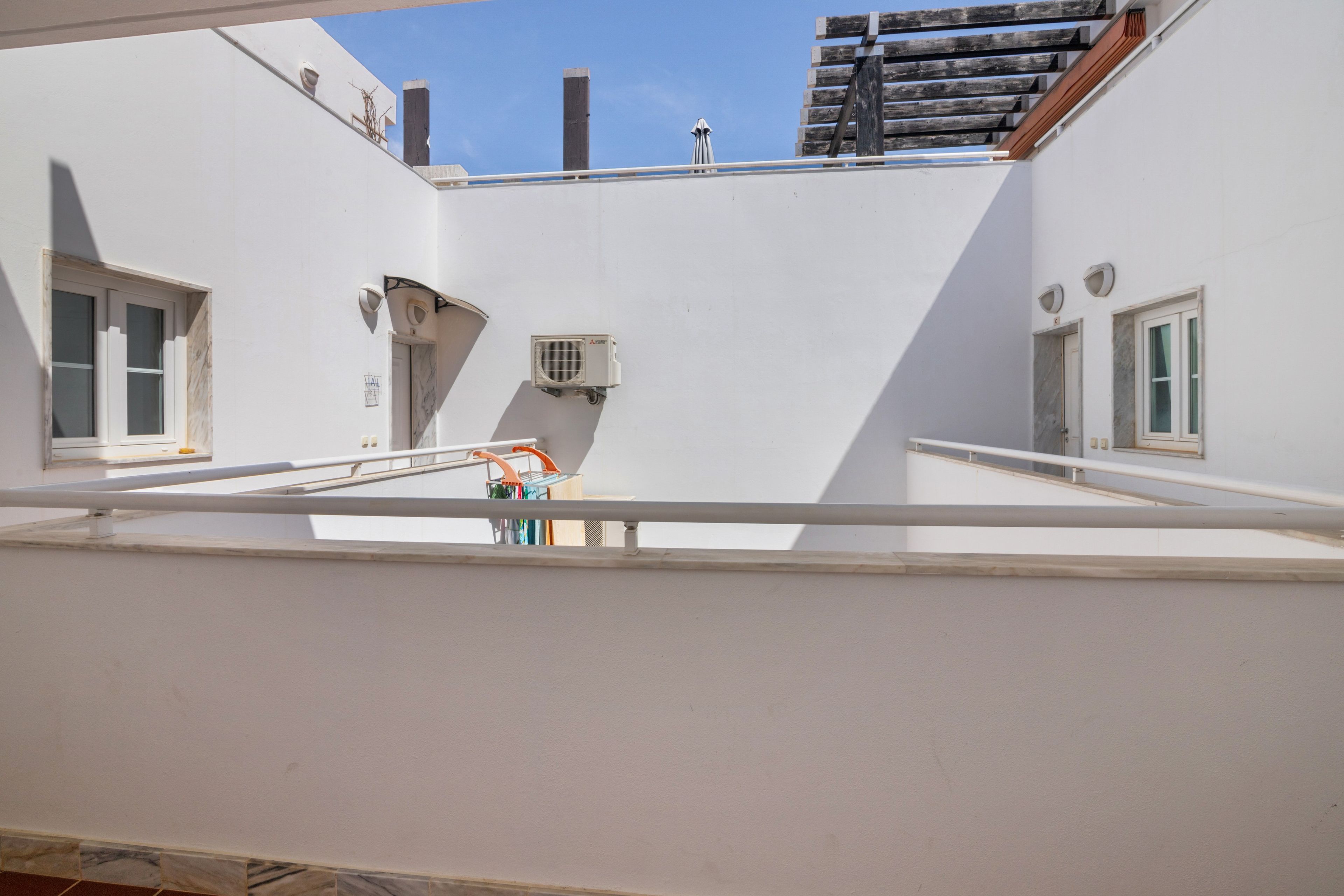A rooftop terrace with a metal railing, a clothes drying rack, and a small air conditioning unit.