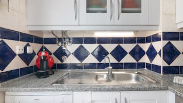 A kitchen with white cabinets, a stainless steel sink, a red coffee maker, and blue and white patterned tiles.