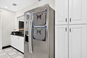 A kitchen with a stainless steel refrigerator, white cabinets, and a tiled floor. - Chompers Den - Walk to the Swamp! (Gainesville)