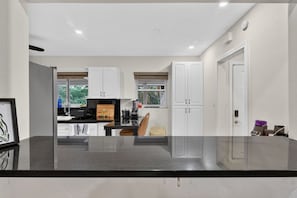 A modern kitchen with white cabinets, a black countertop, and a window with a view of greenery.