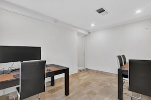 A room with two desks, chairs, a television, and a door leading to another room.