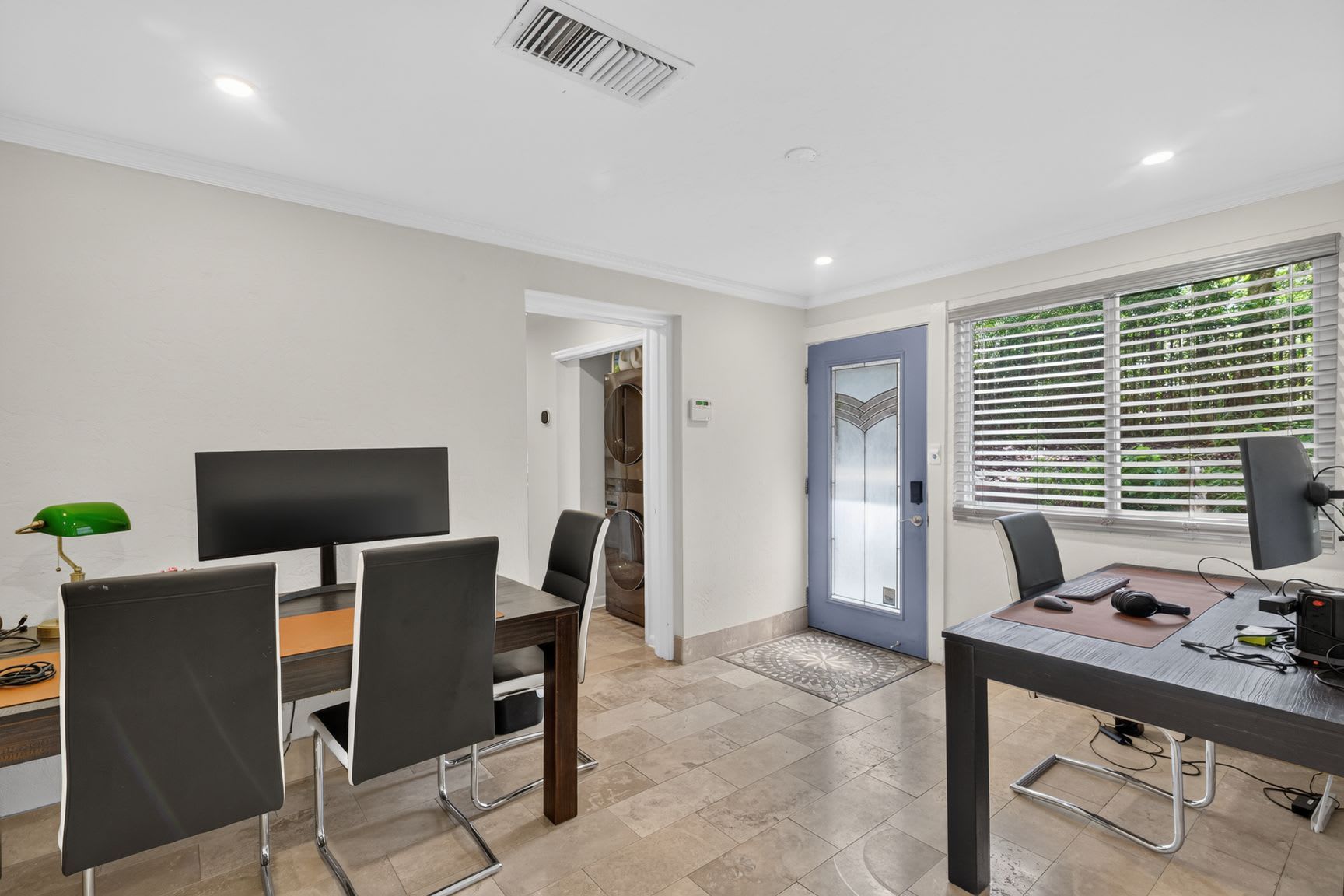 A modern room with a dining area, a computer desk, and a door leading to a kitchen.