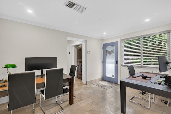A modern room with a dining area, a computer desk, and a door leading to a kitchen.