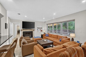 A modern living room with a fireplace, a flat-screen TV, and a large window with blinds. - Chompers Den - Walk to the Swamp! (Gainesville)