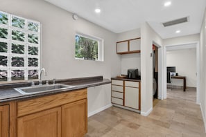 A kitchen with a granite countertop, wooden cabinets, a built-in sink, and a window with a view of trees. - Chompers Den - Walk to the Swamp! (Gainesville)