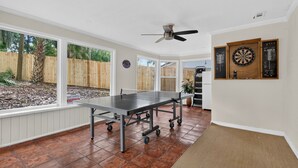 Ein Zimmer mit einem Pongtisch, einem Deckenventilator und Dartscheiben an der Wand.