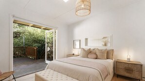 Ein Schlafzimmer mit einem großen Bett, einem Nachttisch, einer Bank und einer Tür, die zu einem Außenbereich führt.