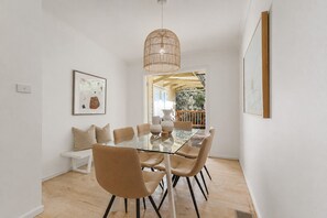 A dining area with a glass table, six chairs, and a hanging light fixture.