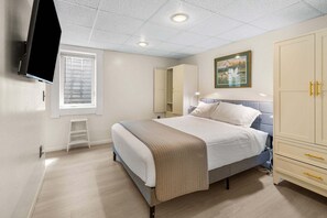Een slaapkamer met een bed, een kledingkast, een televisie, een raam met zonwering en een schilderij aan de muur.