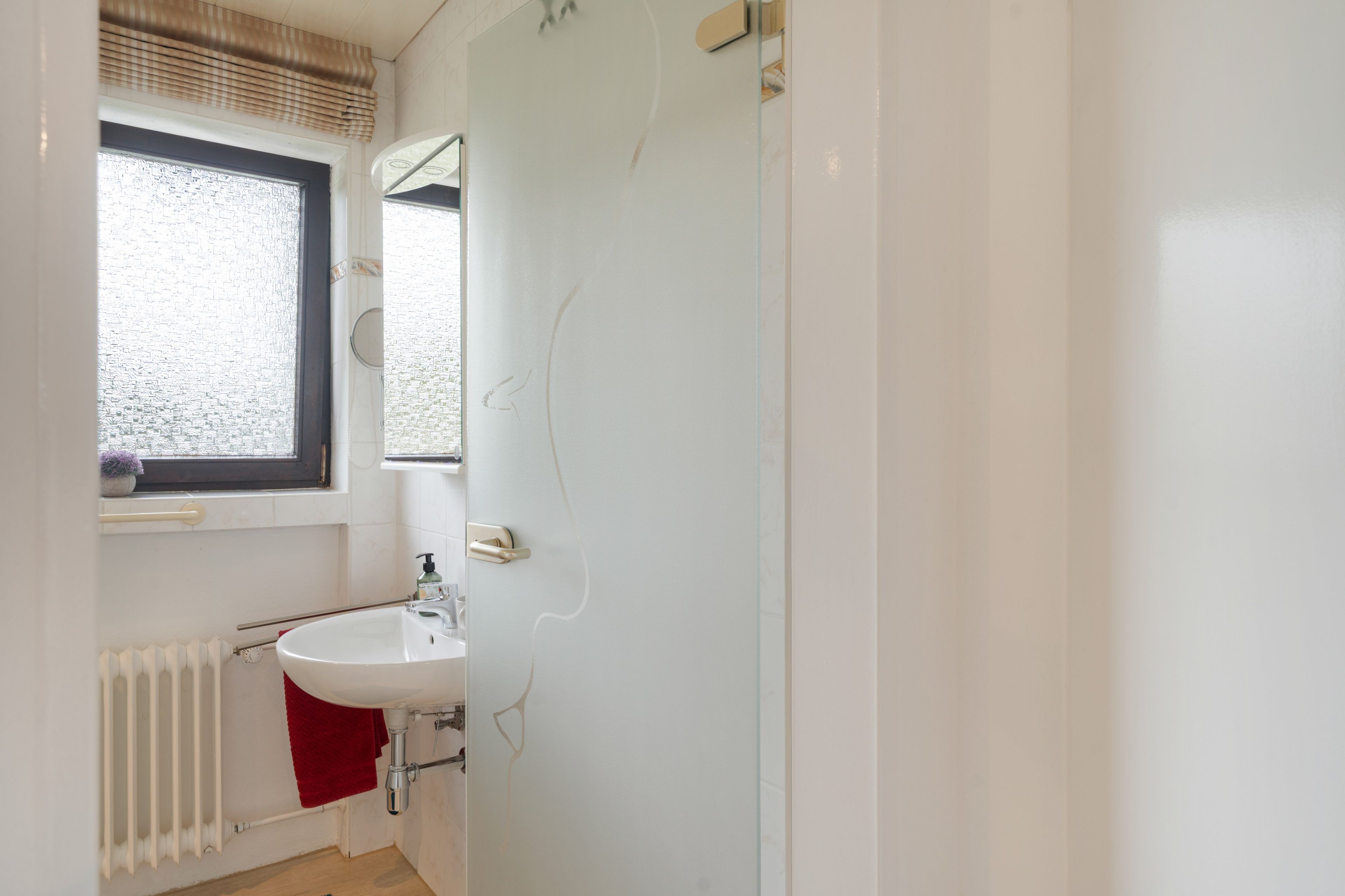 Ein Badezimmer mit einem weißen Waschbecken, einem Fenster mit Jalousien und einem Handtuch an der Heizung.