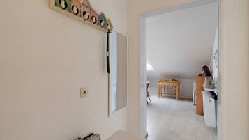 A hallway leading to a dining area with a table and chairs, a bookshelf with books, and a wall-mounted light fixture.