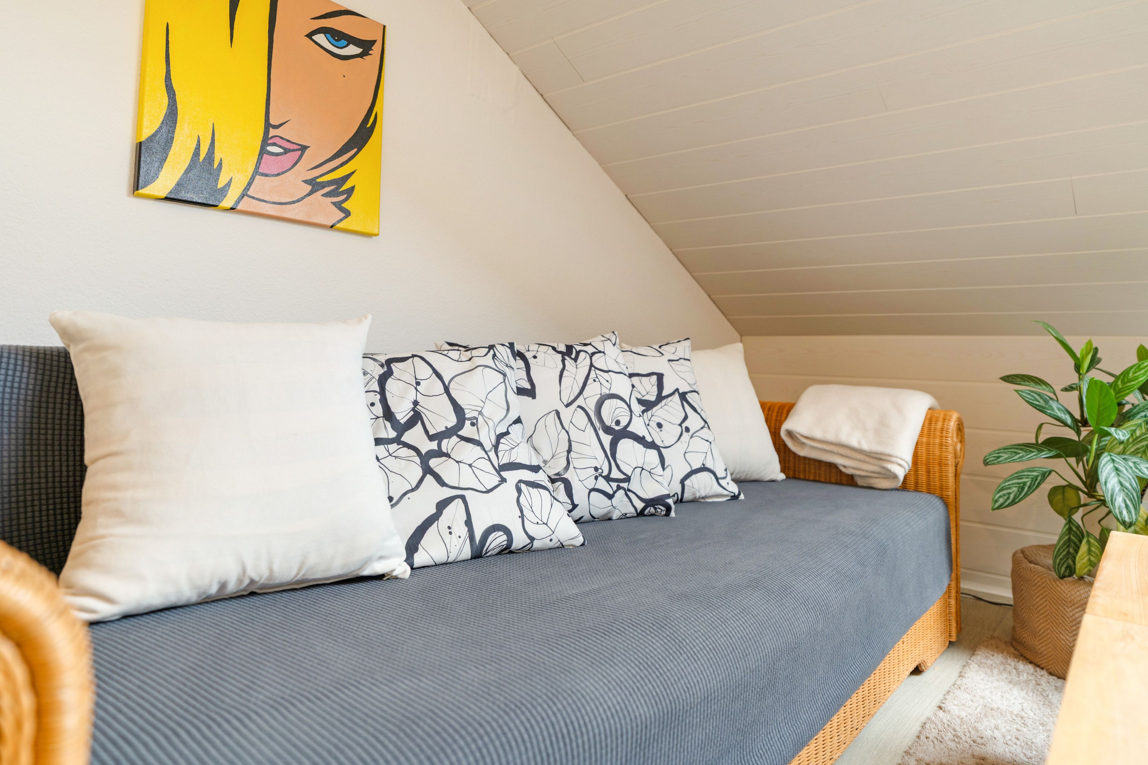 Ein Schlafzimmer mit einem Bett, Kissen, einem Gemälde und einer Pflanze.