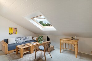 A cozy loft bedroom with a skylight, a sofa, a coffee table, a wicker chair, and a small wooden desk.
