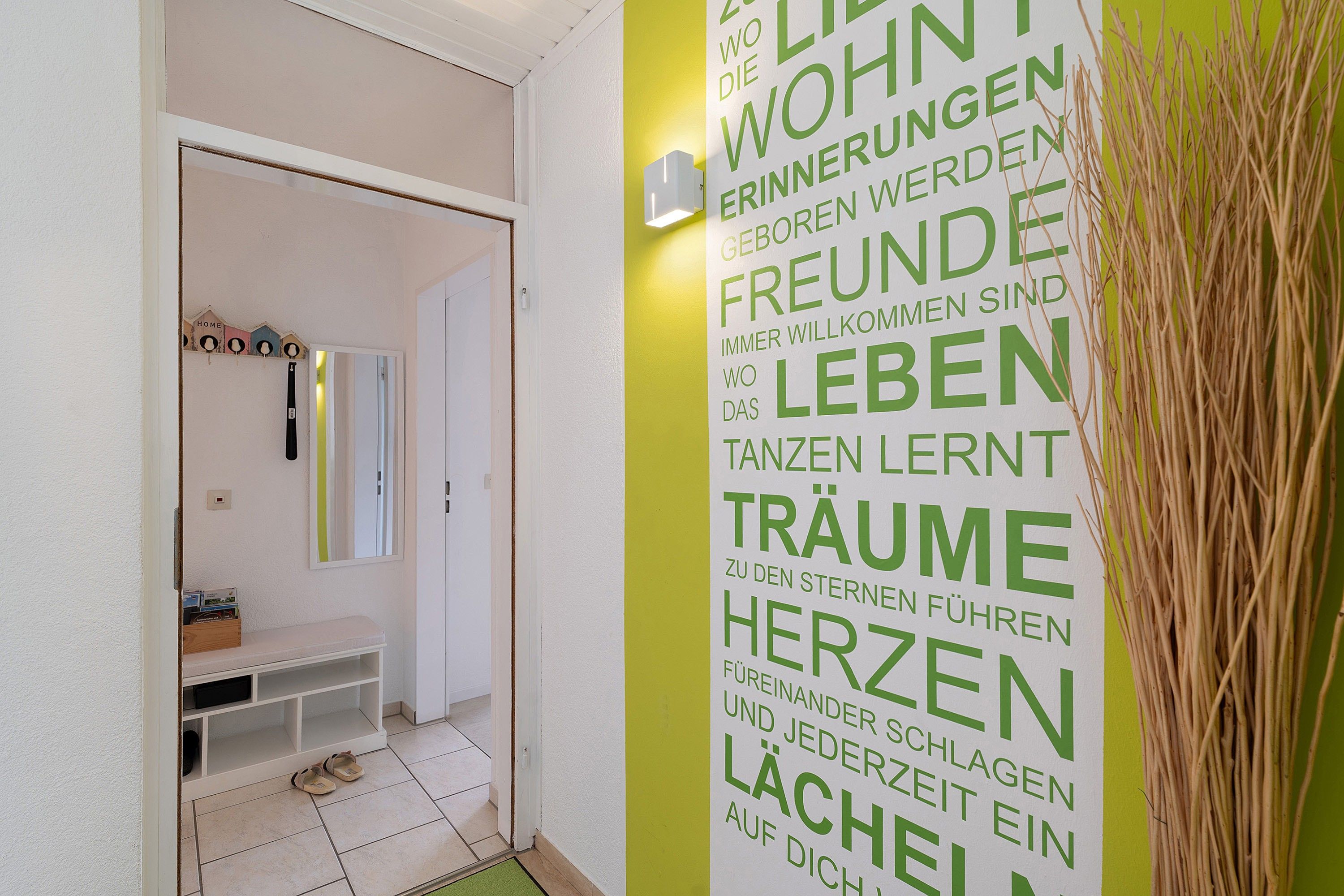 Ein Flur mit einer weißen Tür, die zu einem Raum mit einer Bank und einem Spiegel führt.