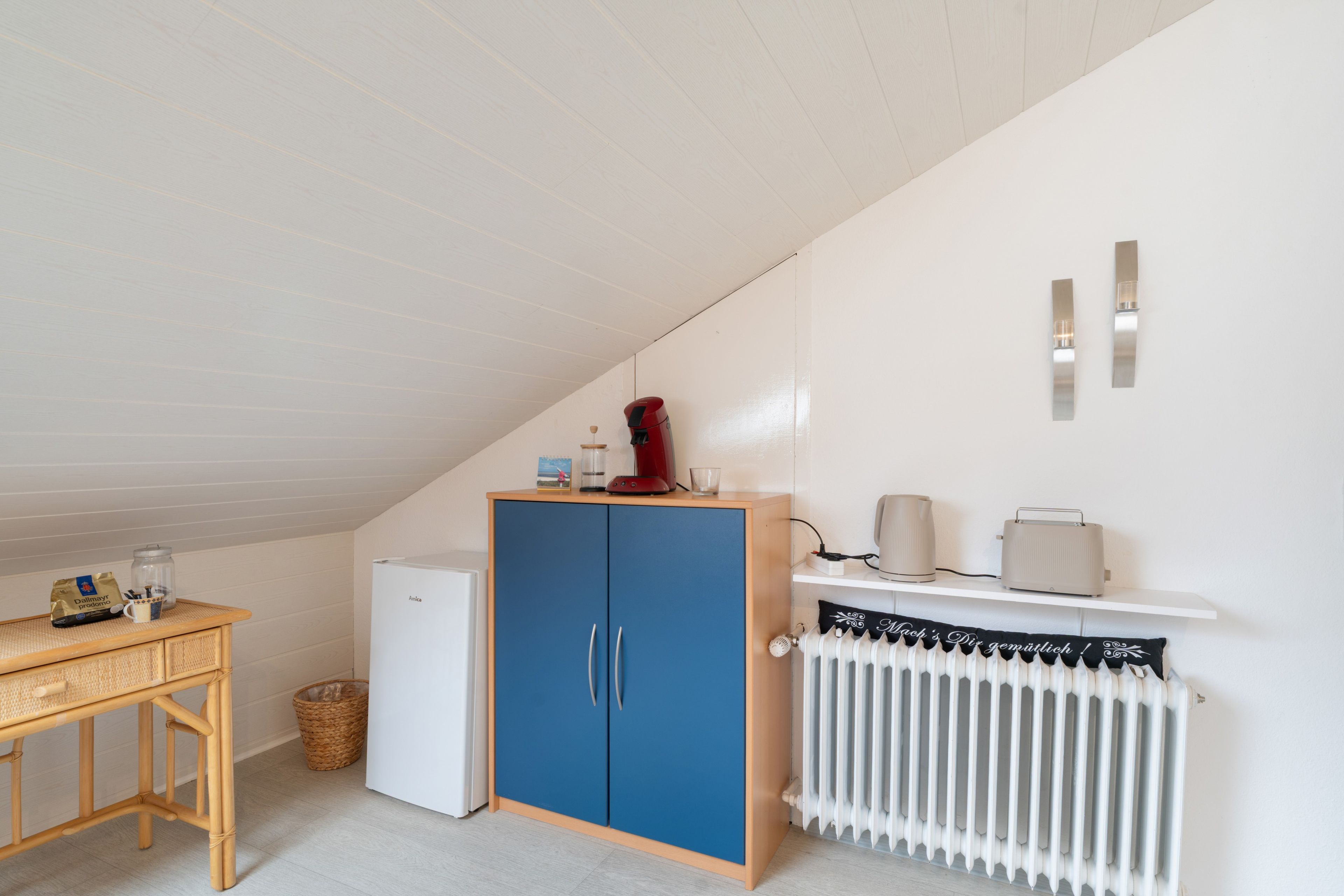 Uma kitchenette compacta com um armário azul, um radiador branco e uma mesa pequena com uma cesta.