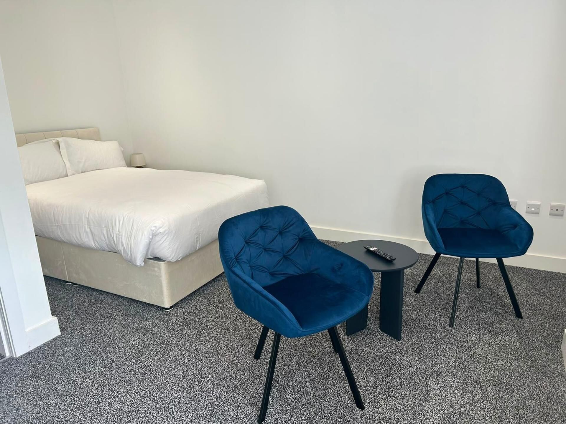 A hotel room with a bed, two chairs, a small table, and a remote control on the table.