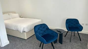 A hotel room with a bed, two chairs, a small table, and a remote control on the table.