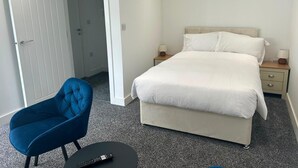 A bedroom with a bed, bedside tables, a chair, and a remote control on a small table.