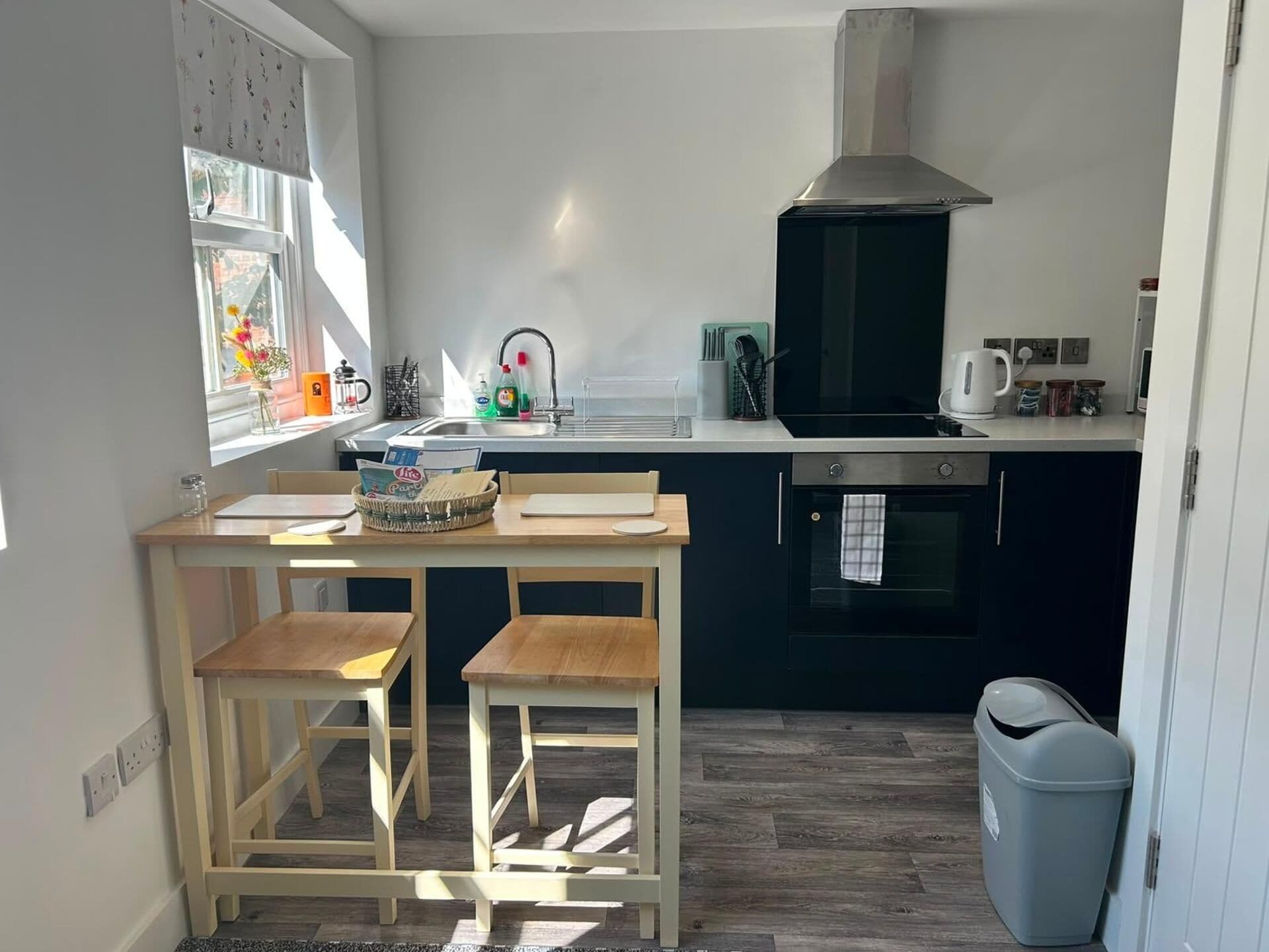 A compact kitchen with a dining table, two chairs, a stove, and a trash bin.