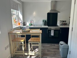 Una cocina compacta con una mesa de comedor, dos sillas, una estufa y un cubo de basura.