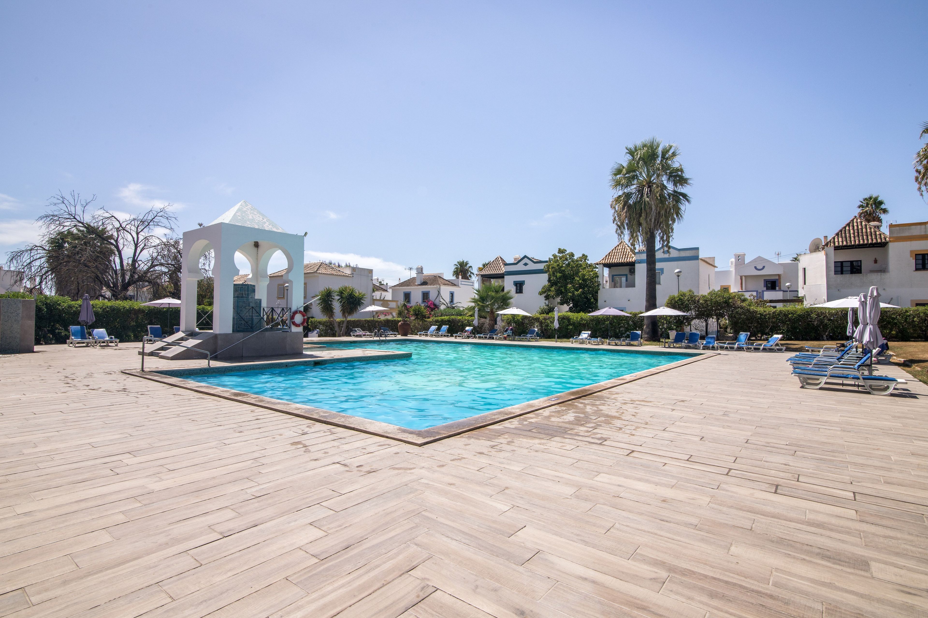 Une piscine dotée d’un pavillon, de chaises longues et de palmiers.