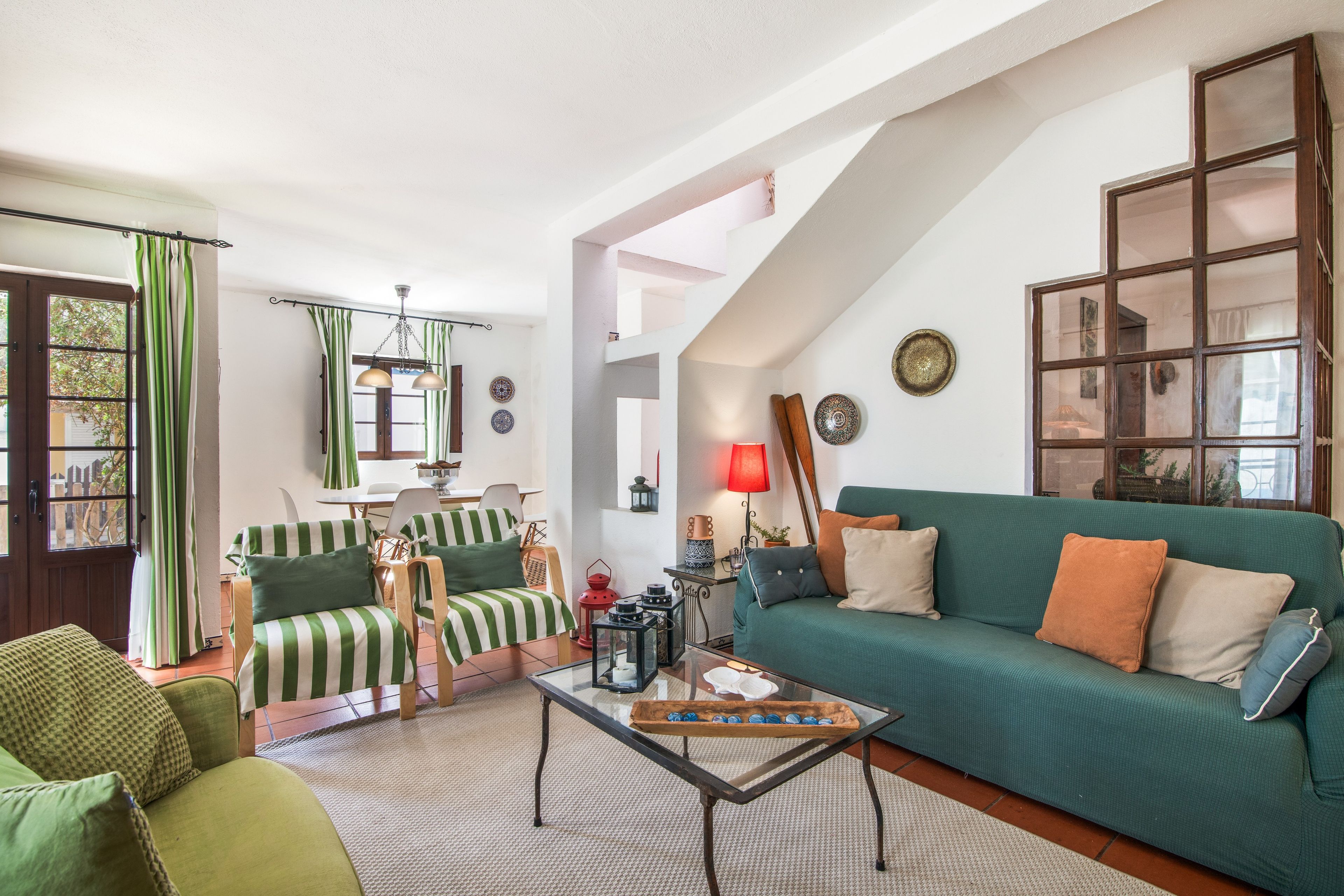 Un salon chaleureux avec un canapé vert, des fauteuils à rayures, une table basse en verre et un coin repas comprenant une table et des chaises.