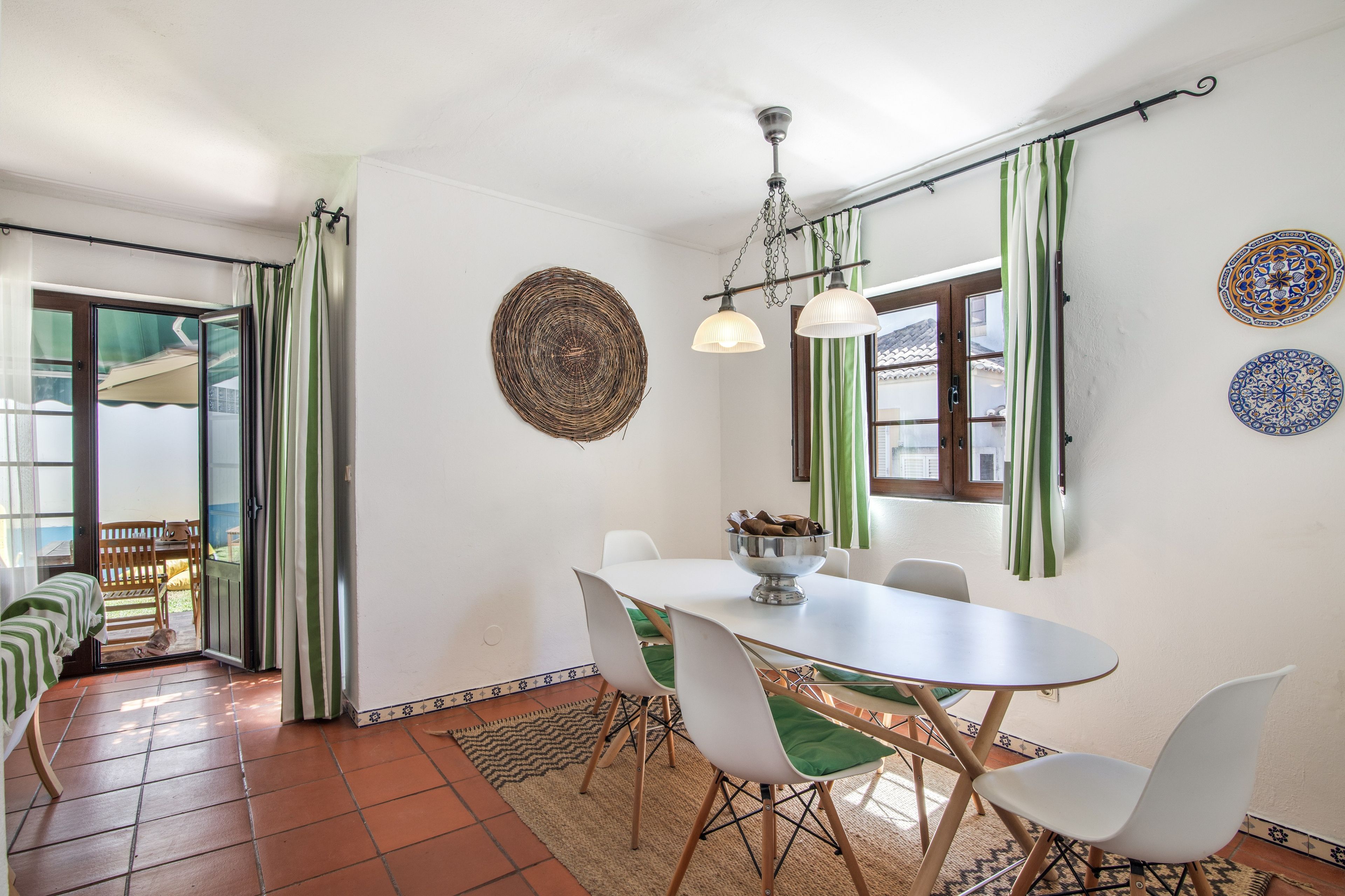 A dining area with a table, chairs, a hanging light fixture, and decorative plates on the wall.