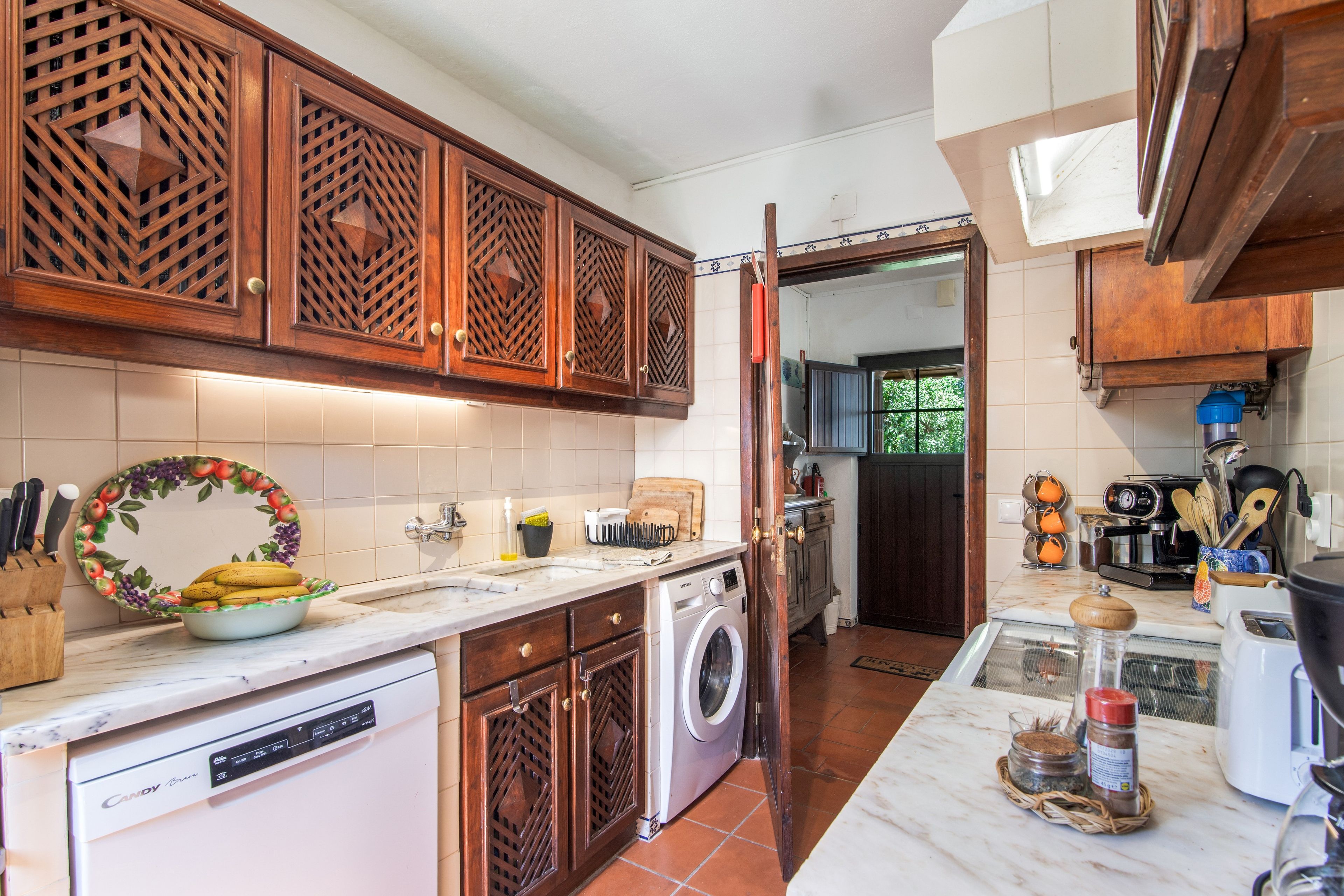 A kitchen with wooden cabinets, a washing machine, a sink, and various kitchen utensils.