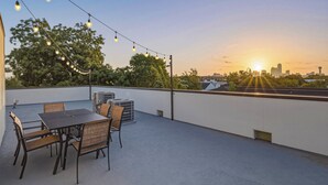 An outdoor seating area with a table and chairs, string lights, and air conditioning units. - Luxe 6BR Duplex | Rooftop, Hot Tubs, Games & Views (Dallas)