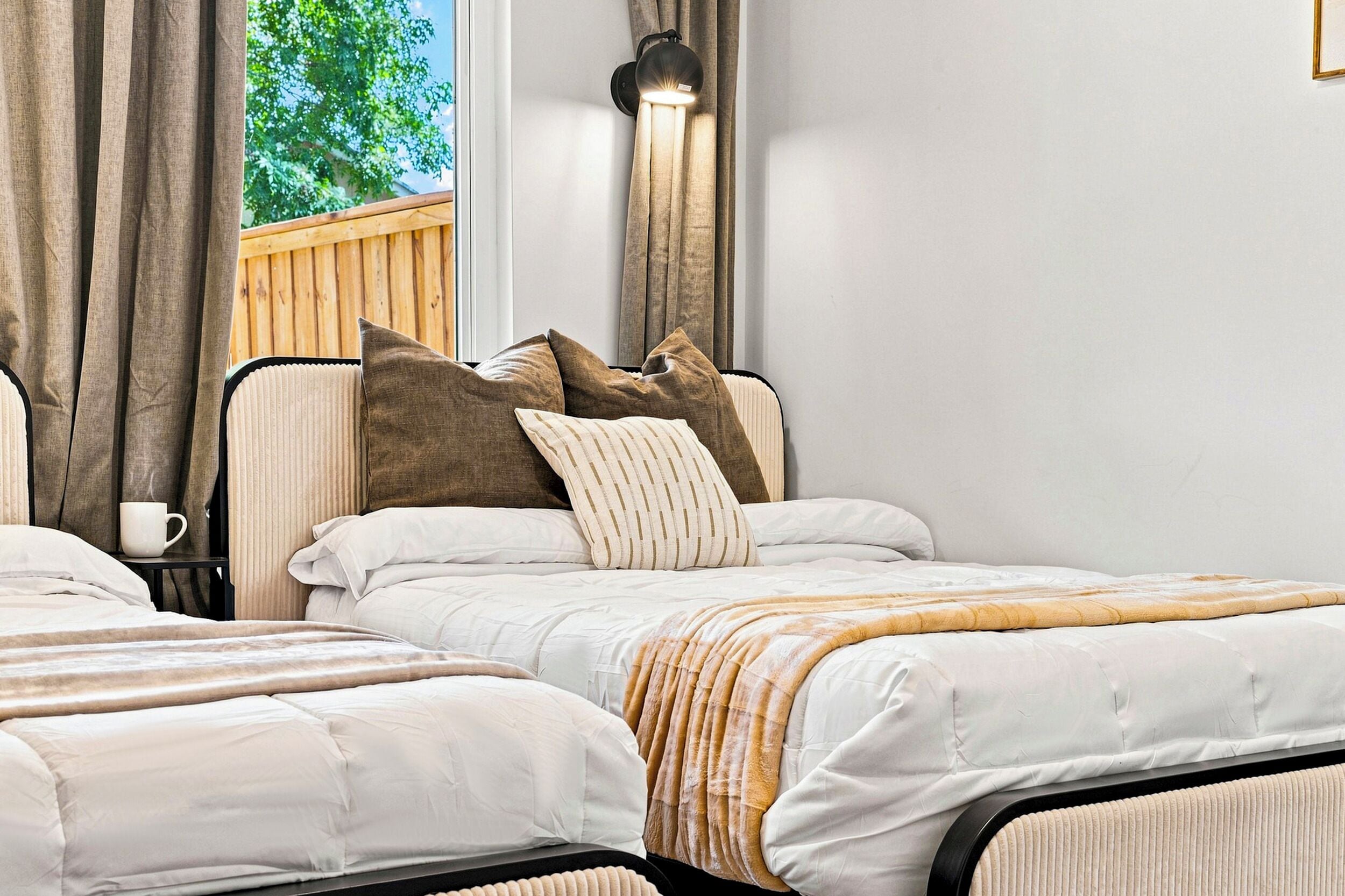 A double bed with a striped throw blanket, a bedside table with a white mug, and a window with curtains.