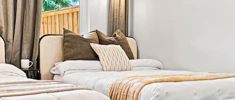 A double bed with a striped throw blanket, a bedside table with a white mug, and a window with curtains.