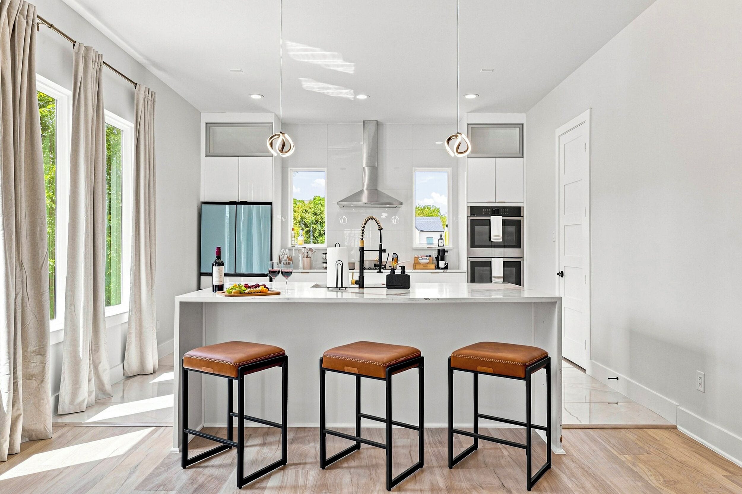 A modern kitchen with a central island, bar stools, and pendant lighting.