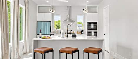 A modern kitchen with a central island, bar stools, and pendant lighting.