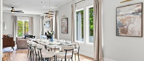Uma sala de jantar moderna com uma mesa comprida posta para seis pessoas, rodeada por cadeiras brancas com estrutura preta.