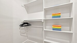 A closet with white shelving and a metal rod for hanging clothes. - Luxe 6BR Duplex | Rooftop, Hot Tubs, Games & Views (Dallas)