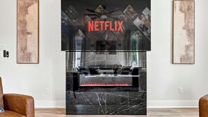 A modern living room with a fireplace, a mounted television, and artwork on the walls. - Luxe 6BR Duplex | Rooftop, Hot Tubs, Games & Views (Dallas)